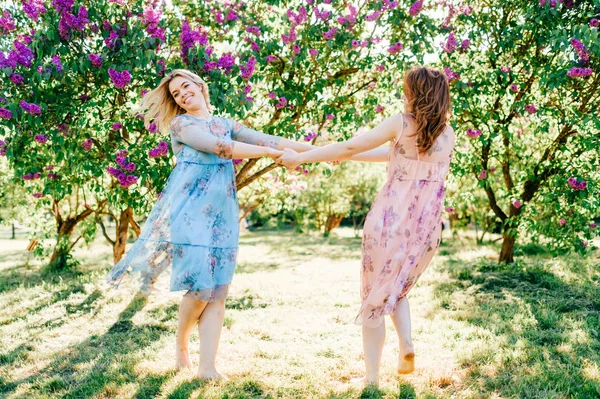 咲くの楽しみを持つ別のドレスの若い双子の姉妹夏の植物園 — ストック写真
