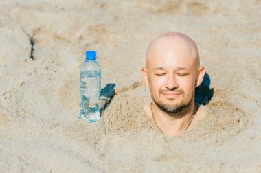 kel adam tarafından su şişe ile plajda kuma gömülü kısmi görünümünü