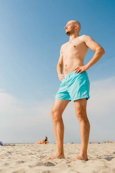 handsome man in blue swimming shorts sunbathing on beach