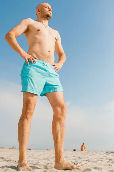 handsome man in blue swimming shorts sunbathing on beach