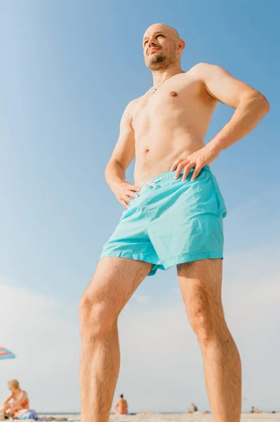 handsome man in blue swimming shorts sunbathing on beach