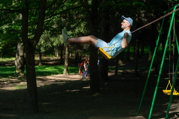 夏の公園の遊び場のブランコに揺れて大人の男 — ストック写真