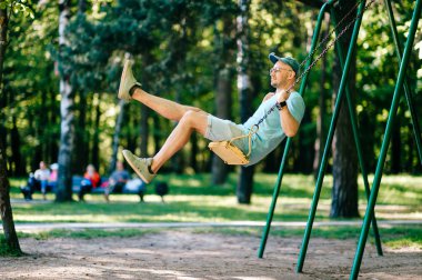 Bahçesi yaz parkta salıncakta sallanan yetişkin adam