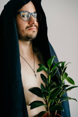 gözlük ve siyah töreni pelerin yeşil bitki potu tutan adam