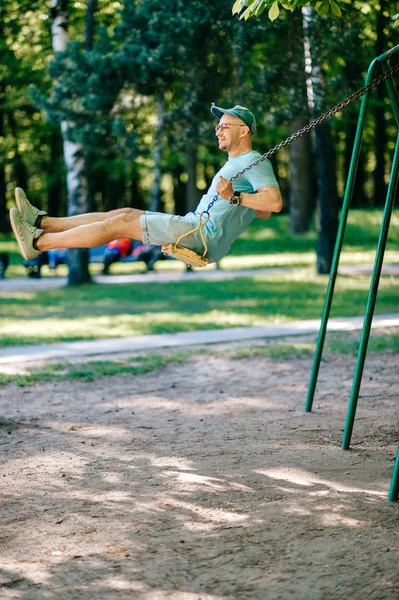 在夏季公园的操场上荡秋千的成年男子 — 图库照片