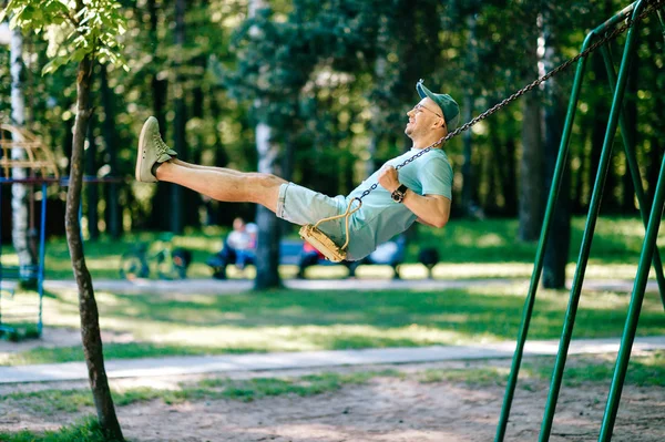 夏の公園の遊び場のブランコに揺れて大人の男 — ストック写真