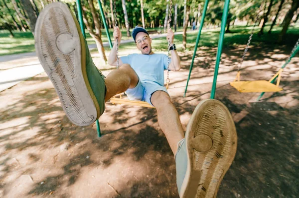 夏の公園の遊び場のブランコに揺れて大人の男 — ストック写真