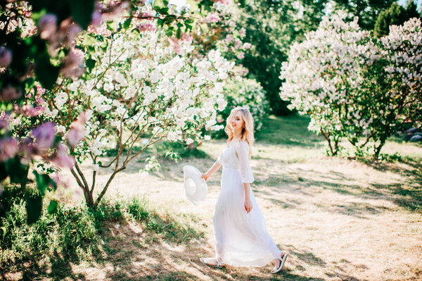 Young pretty blonde woman in white dress in blooming garden