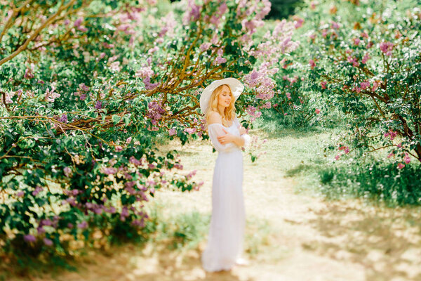 Young pretty blonde woman in white dress in blooming garden