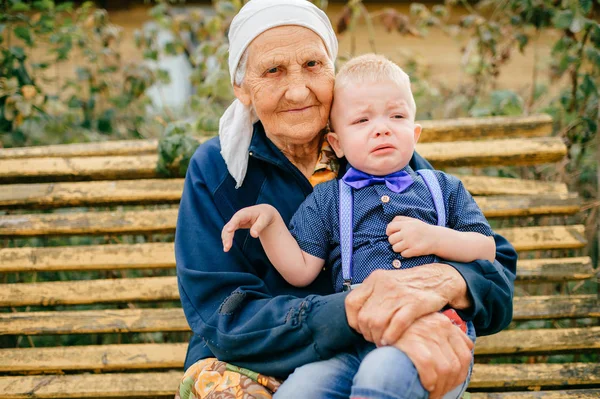 grandmother sitting with crying grandson on bench in yard