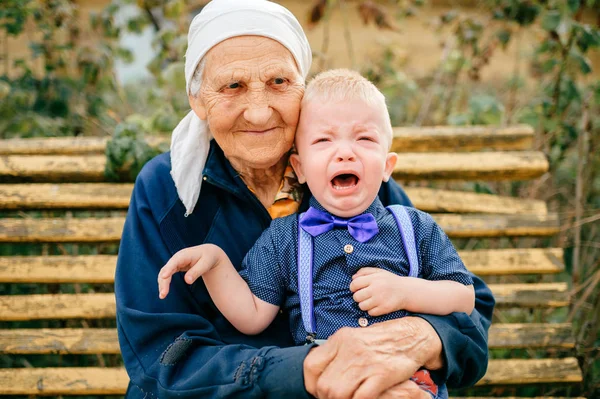grandmother sitting with crying grandson on bench in yard