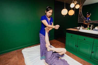 Genç Tay masör işçi kız etnik Asya egzotik kostüm yapar ve mavi gevşeme yoga odasında pembe pijama beyaz güzel bayan için farklı geleneksel spa prosedürler öğeleri gösterir.