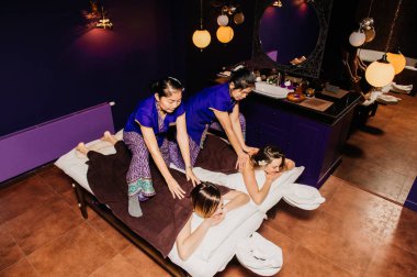 Genç Tay masör işçi kız etnik Asya egzotik kostüm yapar ve mavi gevşeme yoga odasında pembe pijama beyaz güzel bayan için farklı geleneksel spa prosedürler öğeleri gösterir.