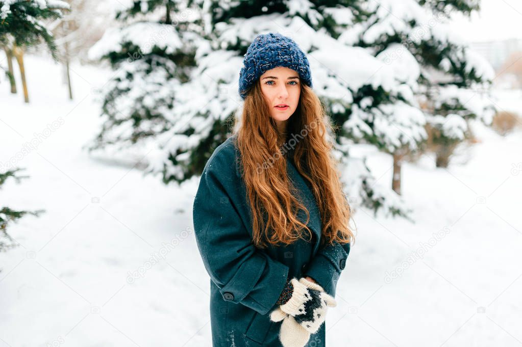Young beautiful woman posing in snowy forest on winter day