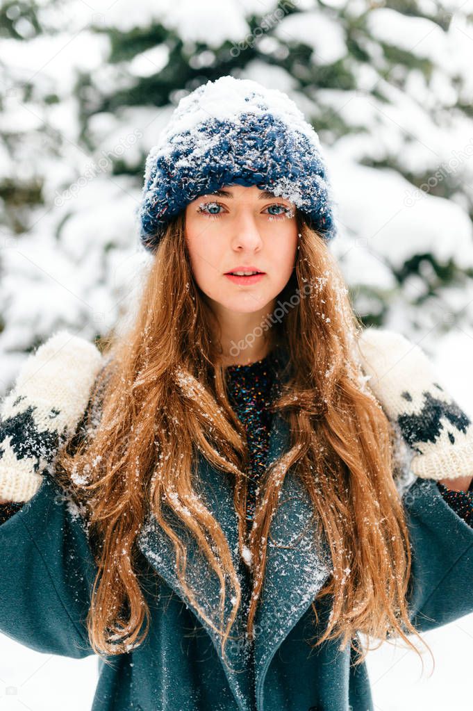 Young beautiful woman posing in snowy forest on winter day