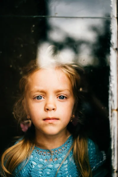 little girl in blue knitted dress looking through window