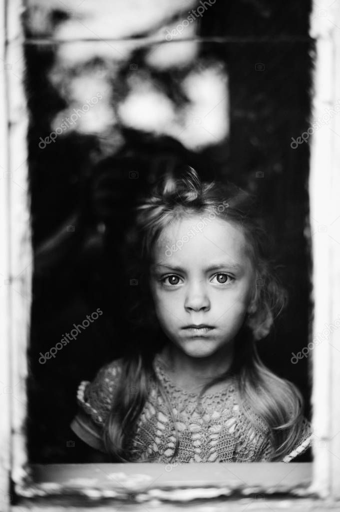 black and white photo of little girl in looking through window