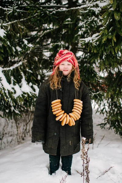 雪覆われた雪のトウヒの背景に首にベーグルの束を持つ少女 — ストック写真