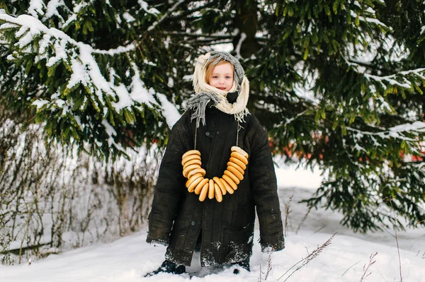 雪覆盖的小女孩与一堆百吉饼在脖子上的雪云杉树背景 — 图库照片