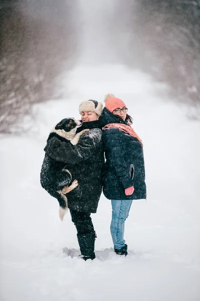 women in warm clothing with dog in winter snowy forest