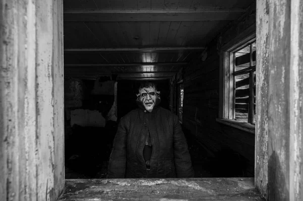 black and white photo of person in creepy mask in wooden house