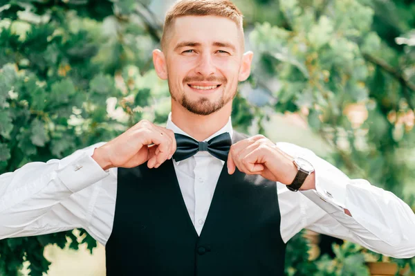 young groom with bow tie on neck standing outdoors