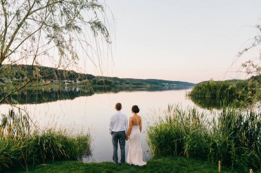 Gölün kıyısında akşam günbatımında ayakta düğün töreninden sonra gelin ve damat görünümünü geri