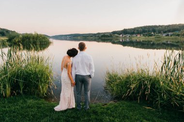 Gölün kıyısında akşam günbatımında ayakta düğün töreninden sonra gelin ve damat görünümünü geri