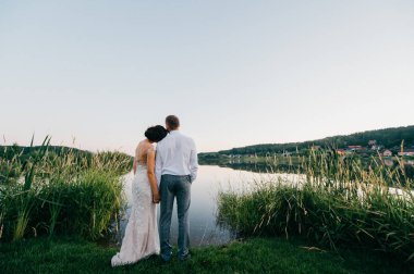 Gölün kıyısında akşam günbatımında ayakta düğün töreninden sonra gelin ve damat görünümünü geri