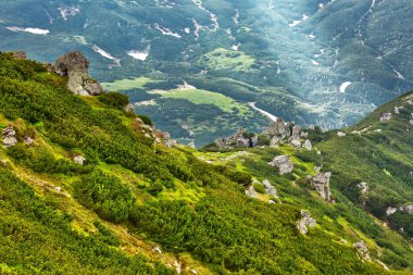Bulutların arasından gün batımında parlayan ışık ışını ile taşlı dağ manzarası