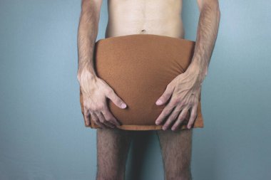 A young naked man covers his penis with a pillow.