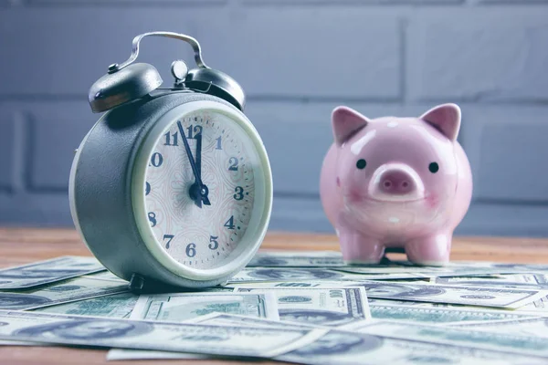 Pink piggy bank beside alarm clock