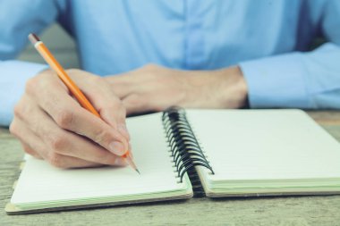 genç bir adam bir kalemle bir defter üzerinde yazıyor.