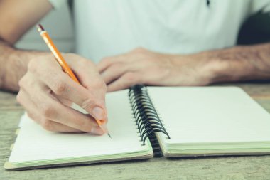 genç bir adam bir kalemle bir defter üzerinde yazıyor.