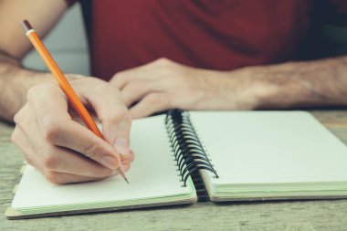 genç bir adam bir kalemle bir defter üzerinde yazıyor.