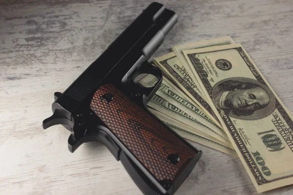 Una pistola con dinero en una mesa de madera —  Fotos de Stock