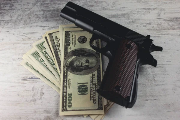 Una pistola con dinero en una mesa de madera —  Fotos de Stock