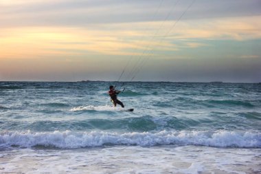 Genç sörfçü gün batımında dalgalara biner.