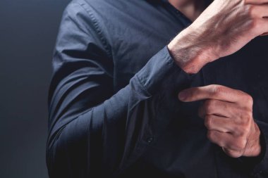 Siyah arka planda gömleğini düzelten bir adama yaklaş..