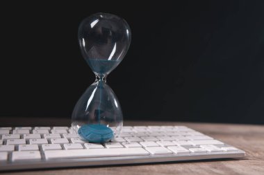 Kum saati ve bilgisayar klavyesi ahşap masada. Zaman yönetimi kavramı.