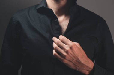 Gömleğinin düğmelerini koyu arkaplanda açan bir adama yaklaş.