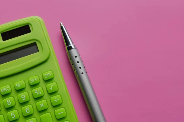 The calculation of the budget, taxes and the cost of the calculator on a pink background. Top view of calculator with pen .