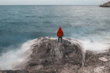 Deniz kenarında, kırmızı kapüşonlu bir kayanın üzerinde.