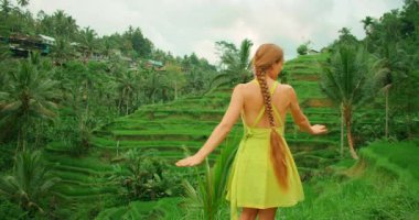 Bali 'de yaz mevsiminde gür pirinç teraslarının önünde neşeyle dans eden elbiseli bir kadın..