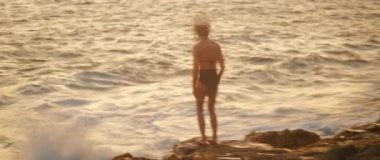 Gün batımında dans gösterisi sırasında okyanusa bakan bir kadın..