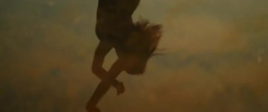 Gün batımında su yüzeyinde yansıyan kayaların üzerinde dans eden kadın silueti..