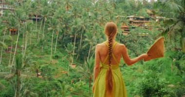 Kadın, Bali 'deki pirinç teraslarının ve palmiye kaplı yamacın manzarasını seviyor..