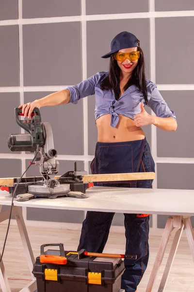 Çekici kadın marangoz bir atölyede yaptığı iş için bazı elektrikli aletler kullanarak