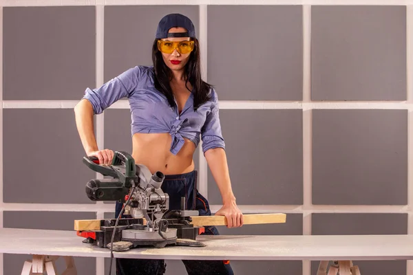 Çekici kadın marangoz bir atölyede yaptığı iş için bazı elektrikli aletler kullanarak