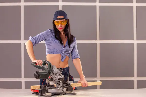 Çekici kadın marangoz bir atölyede yaptığı iş için bazı elektrikli aletler kullanarak